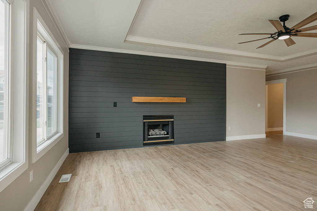 Unfurnished living room featuring wood finished floors, a fireplace, a ceiling fan, ornamental molding, and baseboards
