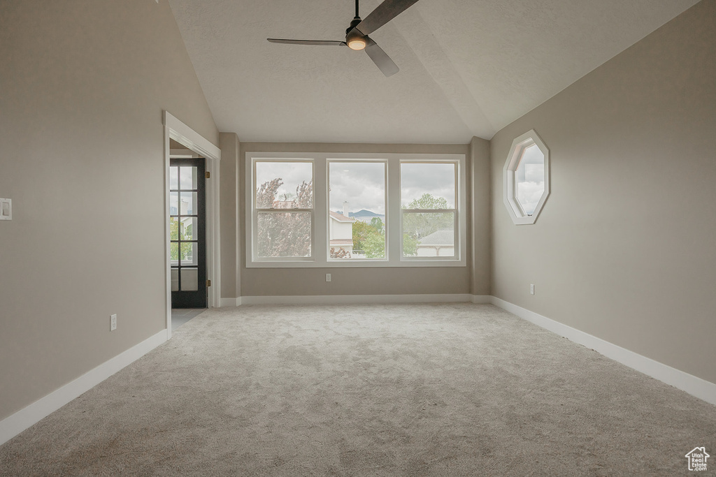 Carpeted empty room with vaulted ceiling, ceiling fan, plenty of natural light, and baseboards