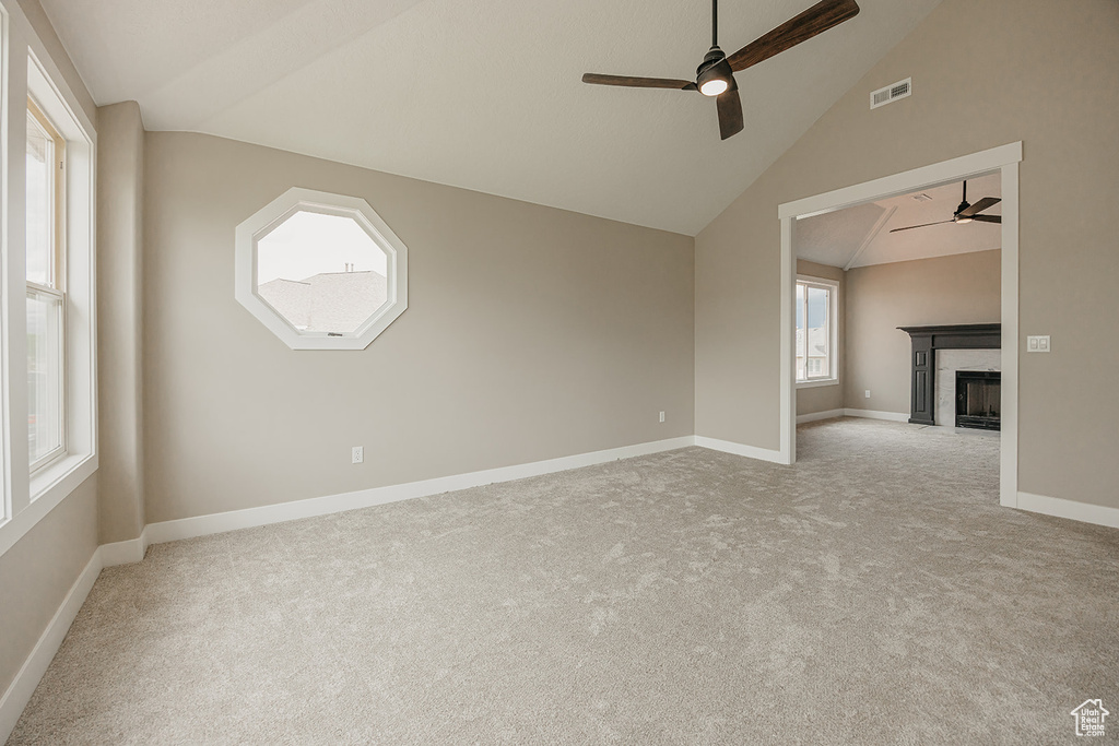 Spare room featuring a ceiling fan, lofted ceiling, carpet flooring, a fireplace, and baseboards