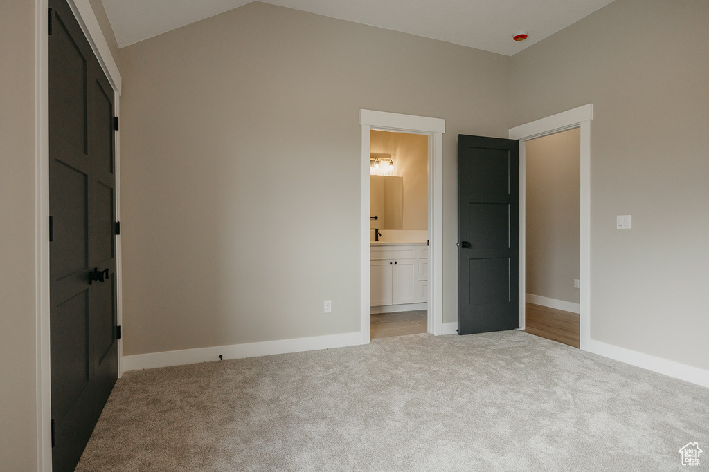 Unfurnished bedroom featuring carpet, baseboards, lofted ceiling, and ensuite bath