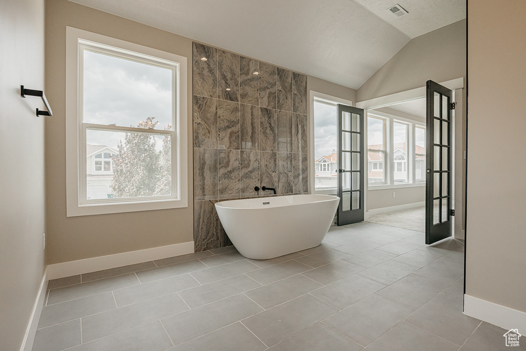 Full bath featuring a freestanding bath, baseboards, tile walls, vaulted ceiling, and french doors