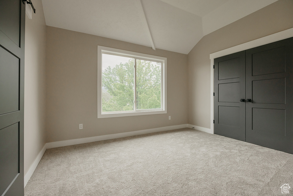 Unfurnished bedroom featuring vaulted ceiling, light colored carpet, and baseboards
