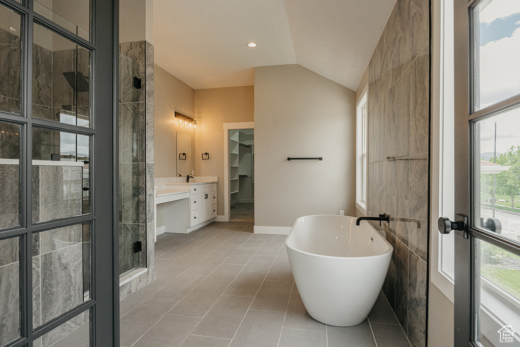 Bathroom featuring a soaking tub, a walk in closet, tiled shower, lofted ceiling, and tile patterned flooring