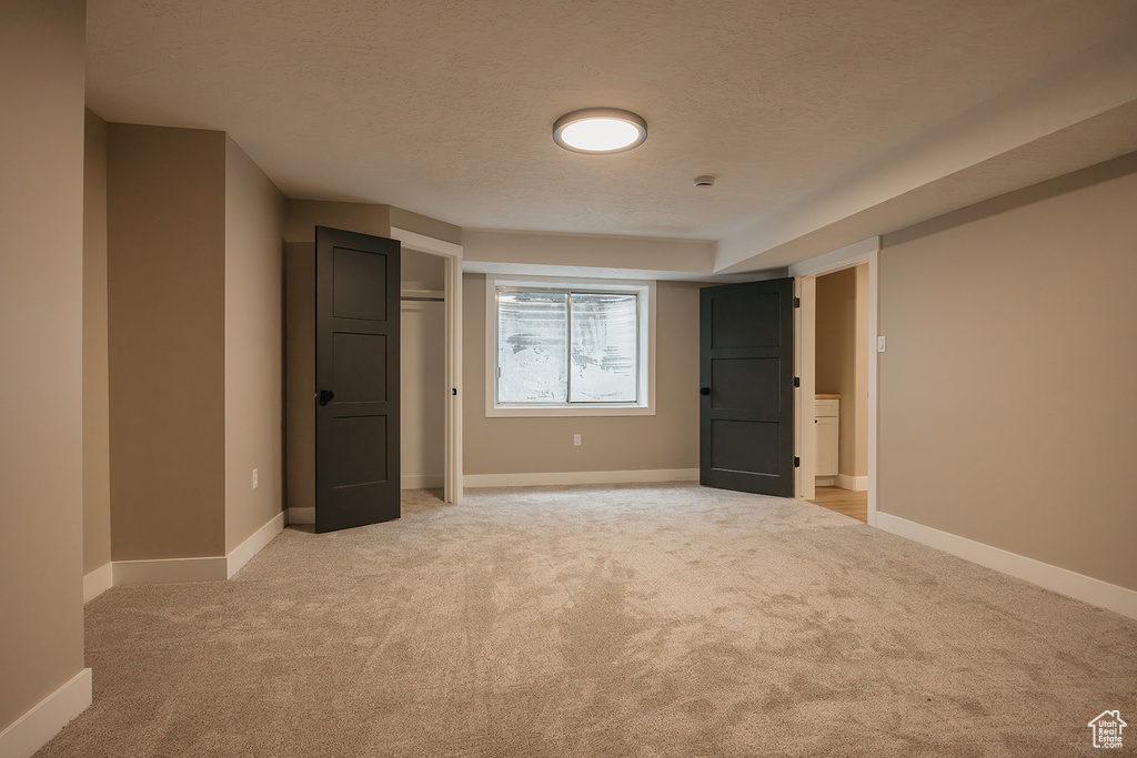 Unfurnished bedroom with light colored carpet, a textured ceiling, baseboards, and a closet