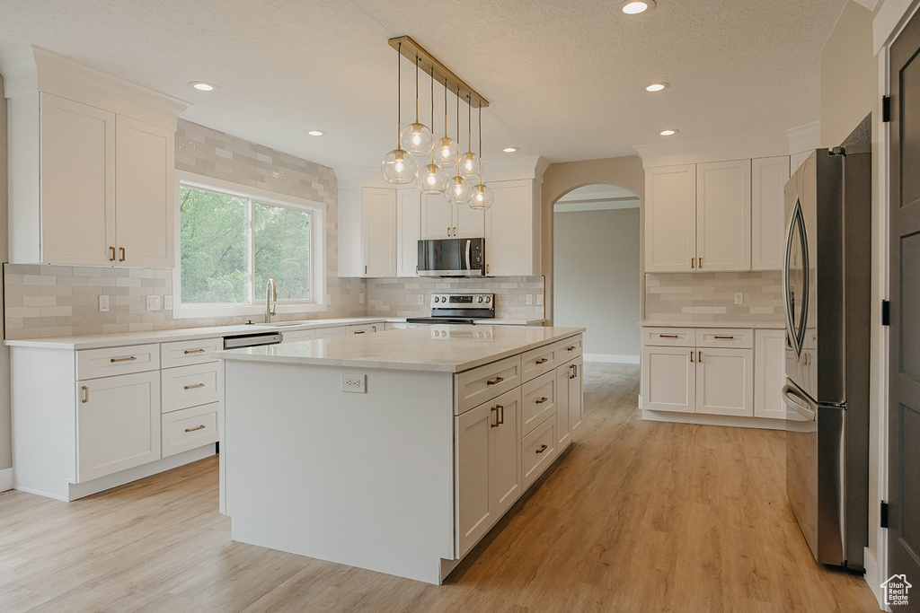 Kitchen featuring stainless steel appliances, arched walkways, white cabinetry, a sink, and backsplash