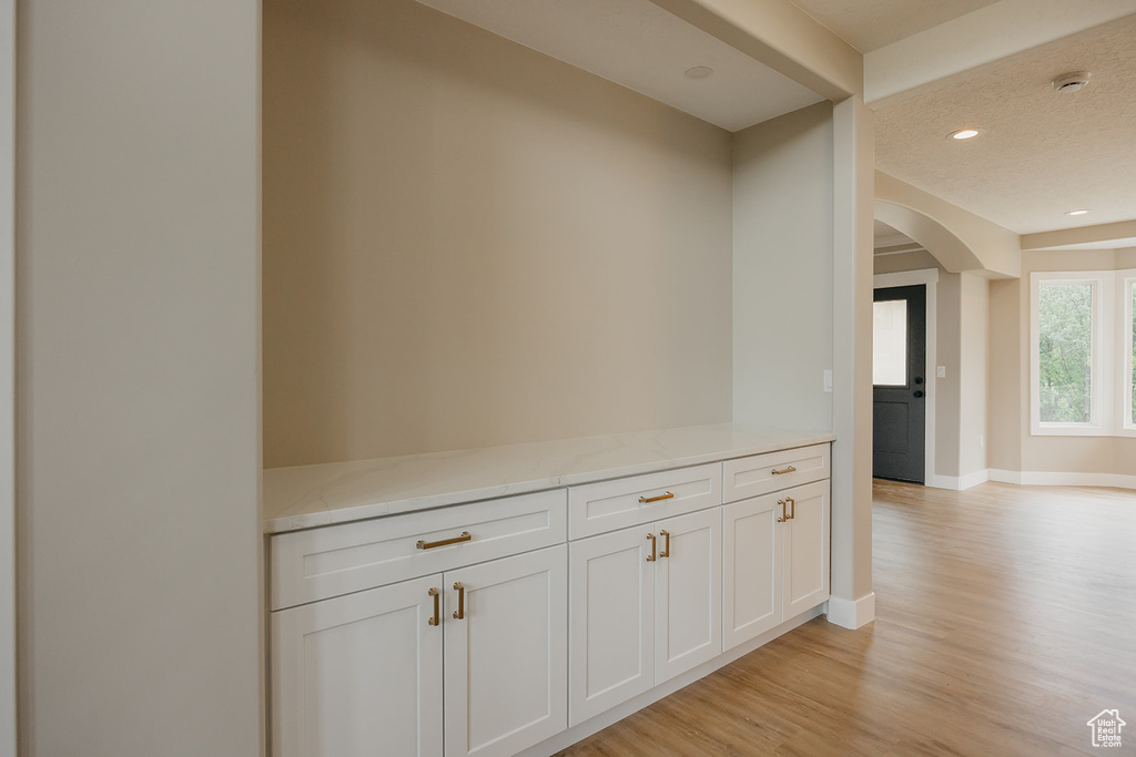 Hall with arched walkways, light wood-type flooring, baseboards, and recessed lighting