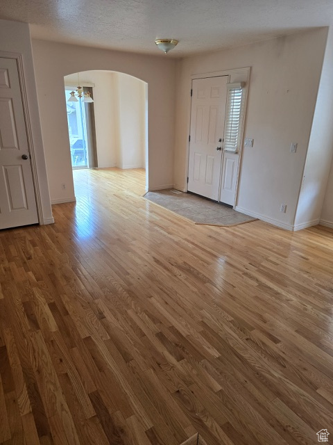 Spare room with arched walkways, light wood-type flooring, baseboards, and a textured ceiling