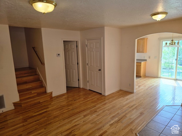 Unfurnished living room with arched walkways, light wood-style flooring, a textured ceiling, a chandelier, and stairway