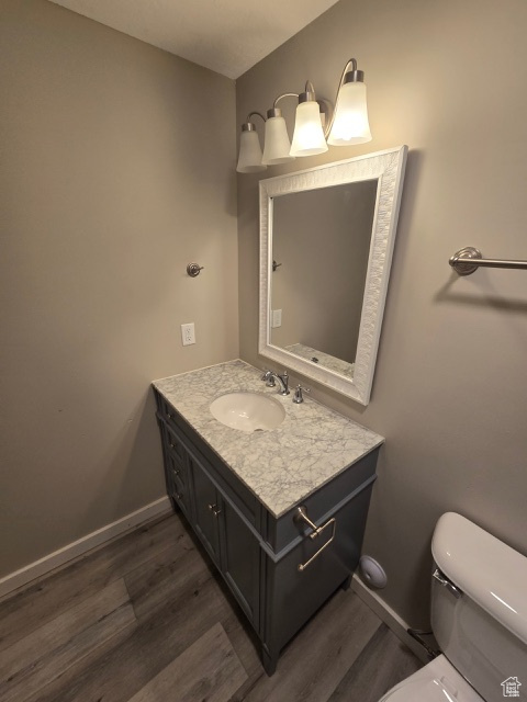 Half bath with wood finished floors, baseboards, vanity, and toilet
