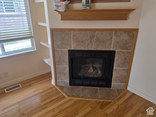 Detailed view of wood finished floors, a tiled fireplace, and baseboards
