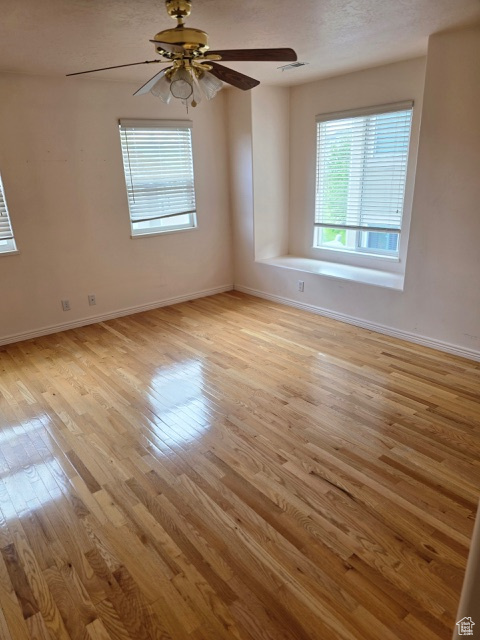 Empty room featuring healthy amount of natural light, light wood finished floors, baseboards, and a ceiling fan