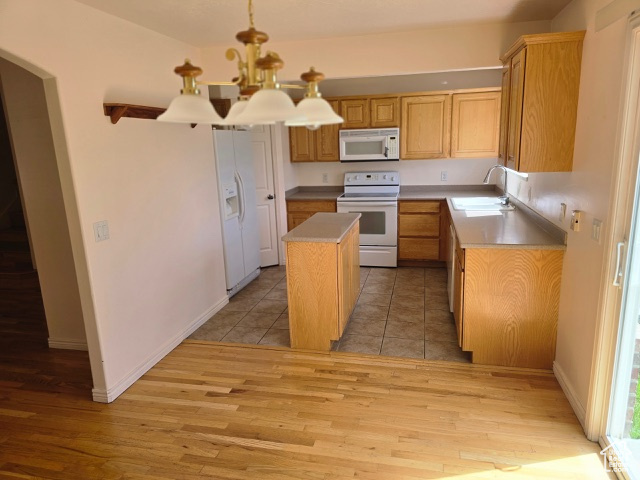Kitchen with white appliances, a sink, a kitchen island, light wood-type flooring, and a chandelier