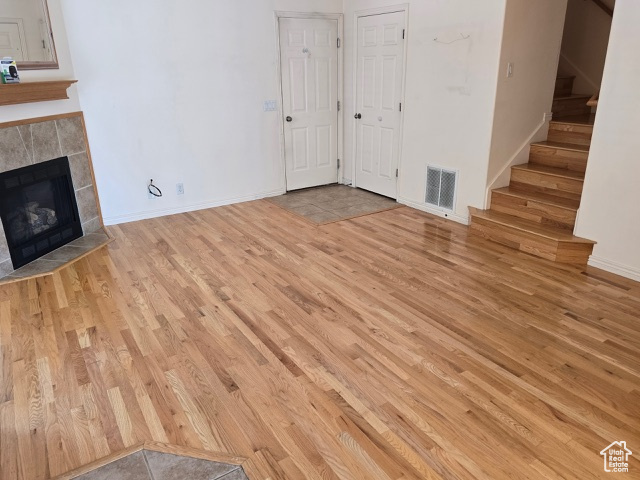 Unfurnished living room featuring wood finished floors, stairs, a tile fireplace, and baseboards