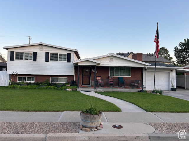 Tri-level home featuring a porch, a garage, a front yard, and concrete driveway