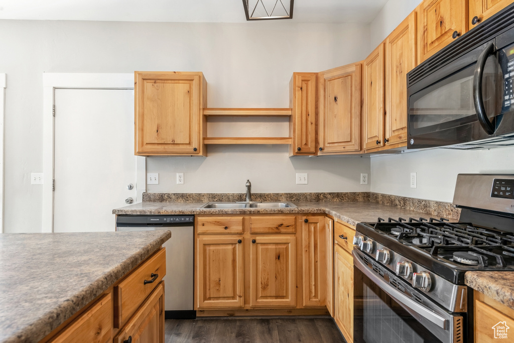Kitchen with stainless steel appliances, a sink, dark countertops, and dark wood finished floors