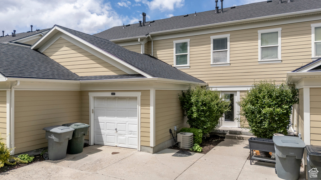 Back of house featuring a garage, driveway, a shingled roof, and central AC unit