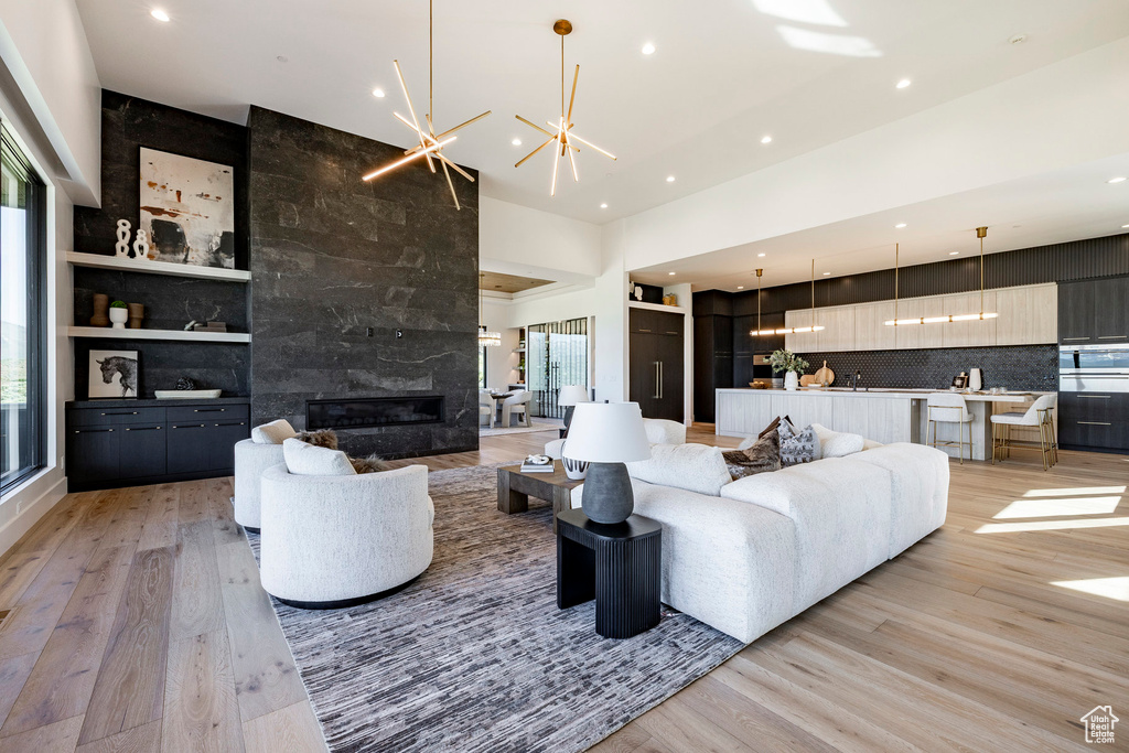 Living room featuring light wood-style floors, recessed lighting, a high ceiling, a chandelier, and a fireplace