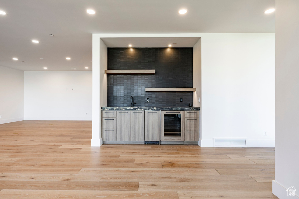 Indoor wet bar with decorative backsplash, light wood-style flooring, recessed lighting, and beverage cooler