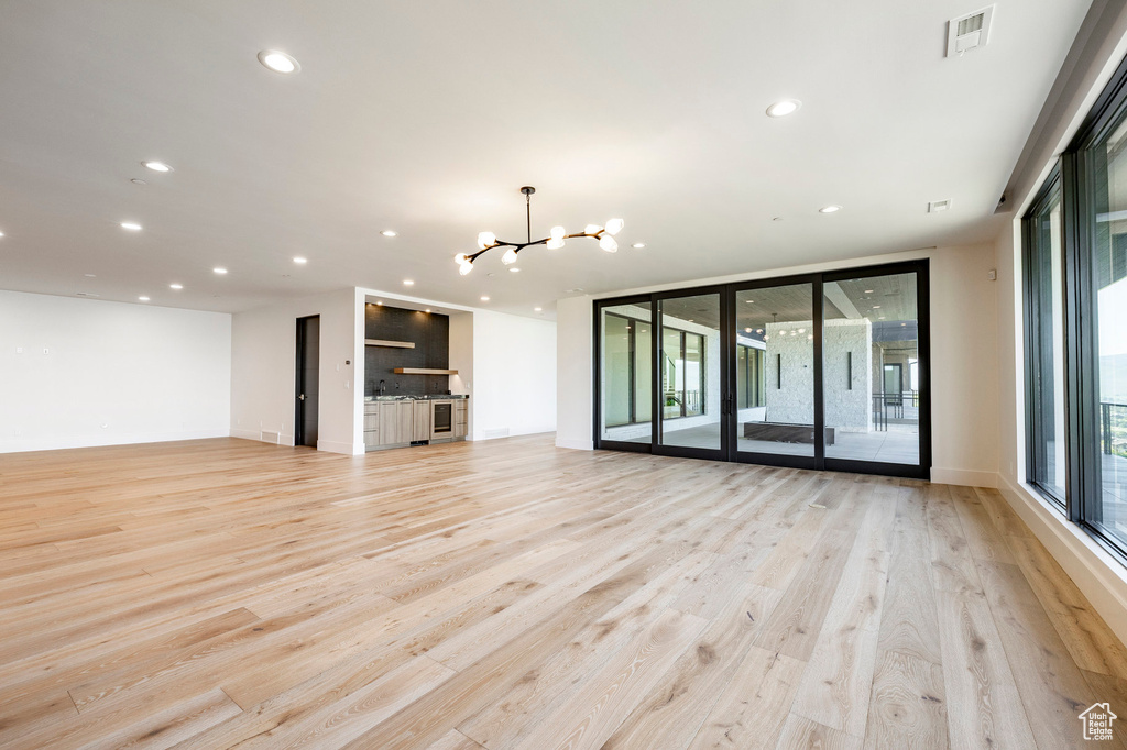 Unfurnished living room with a chandelier, light wood finished floors, floor to ceiling windows, and recessed lighting
