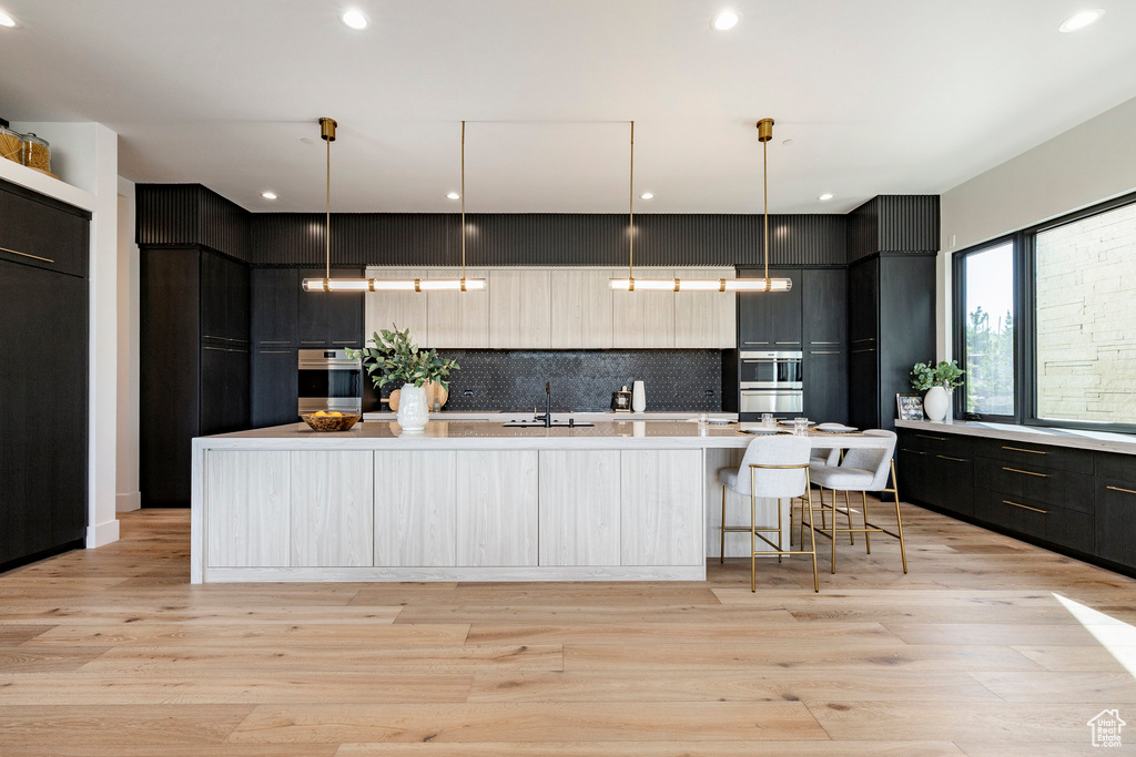 Kitchen with modern cabinets, light countertops, a large island, decorative backsplash, and light wood-type flooring