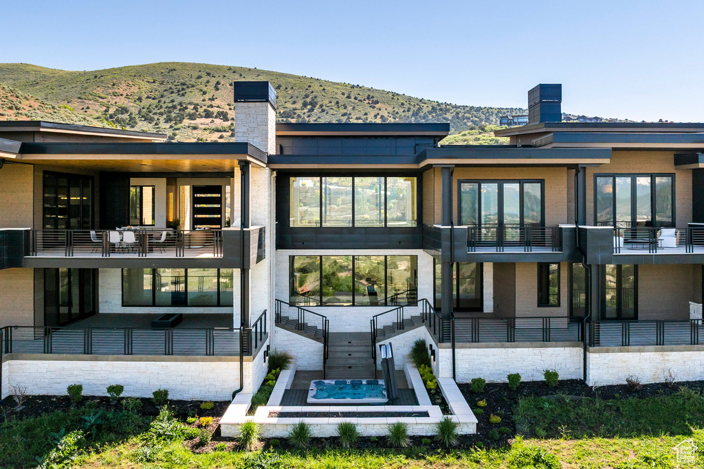 Back of house with a mountain view, a balcony, a chimney, and an outdoor hot tub