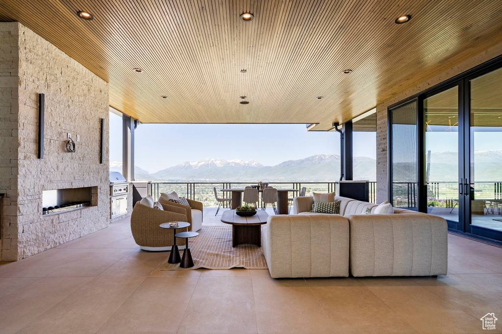 Living room featuring a mountain view, healthy amount of natural light, wood ceiling, an outdoor stone fireplace, and floor to ceiling windows