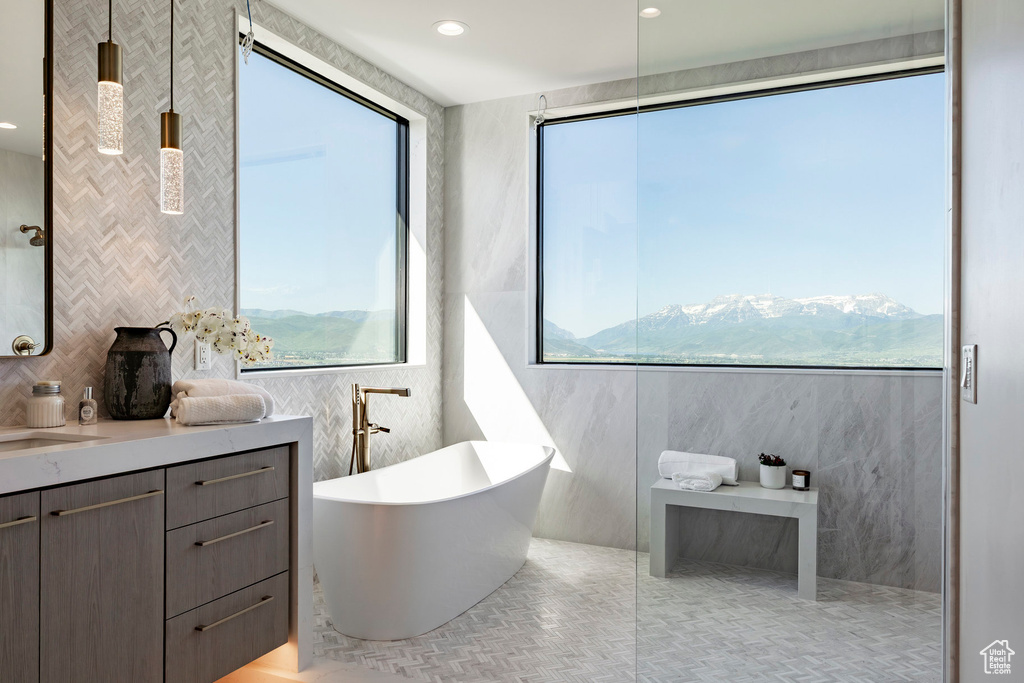 Bathroom featuring tile walls, a freestanding bath, plenty of natural light, vanity, and tile patterned flooring