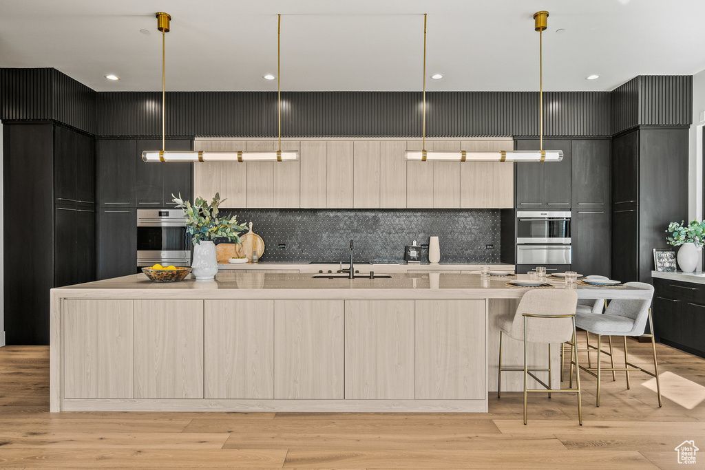 Kitchen with modern cabinets, decorative backsplash, a large island with sink, light countertops, and a breakfast bar area