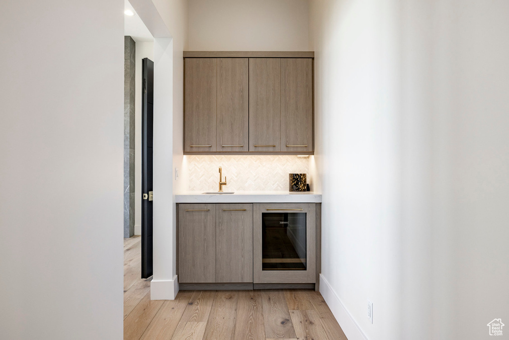 Indoor wet bar featuring light wood-type flooring, decorative backsplash, and wine cooler