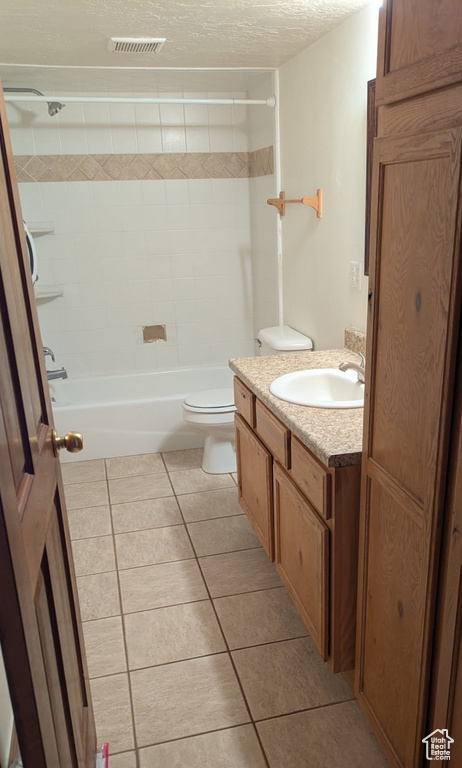 Bathroom with tile patterned flooring, a textured ceiling, toilet, vanity, and bathtub / shower combination