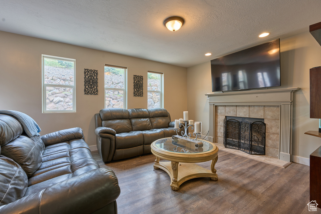 Living room with wood finished floors, recessed lighting, a tiled fireplace, a textured ceiling, and baseboards