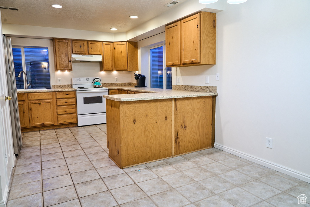 Kitchen with white electric range oven, under cabinet range hood, a sink, a peninsula, and recessed lighting