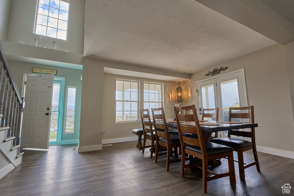 Dining space with a textured ceiling, stairway, healthy amount of natural light, dark wood-style flooring, and baseboards