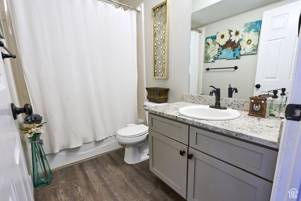 Bathroom with wood finished floors, toilet, shower / bathtub combination with curtain, and vanity