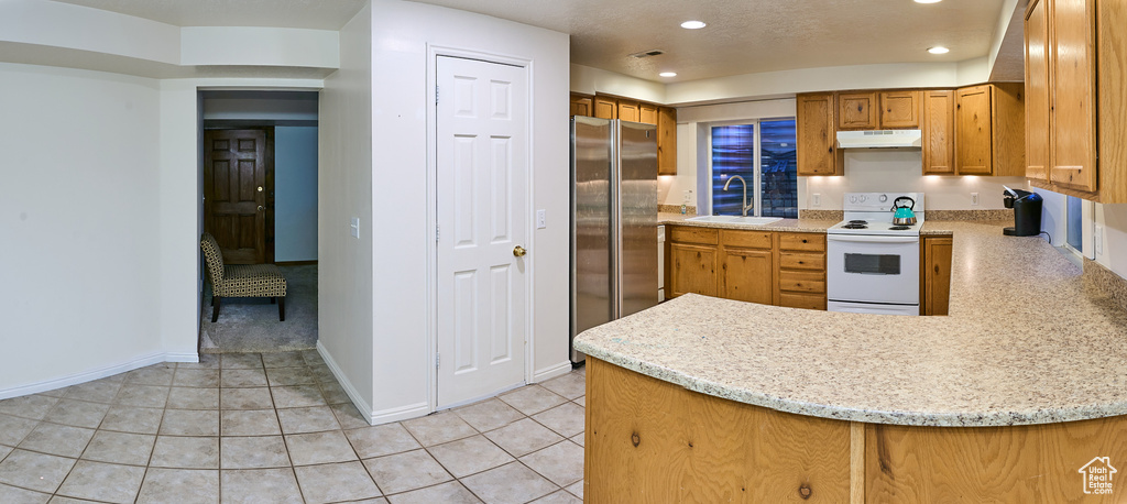 Kitchen with white range with electric cooktop, under cabinet range hood, freestanding refrigerator, a sink, and a peninsula