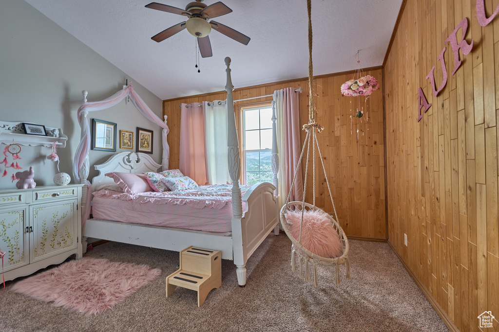 Carpeted bedroom featuring wooden walls and ceiling fan
