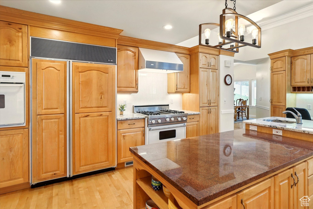 Kitchen featuring wall chimney range hood, high end appliances, a sink, light wood-style floors, and recessed lighting