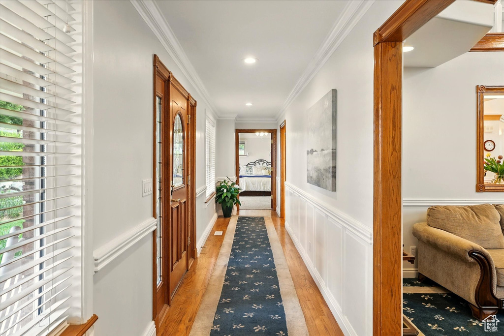 Hall featuring healthy amount of natural light, ornamental molding, light wood-style floors, a wainscoted wall, and recessed lighting
