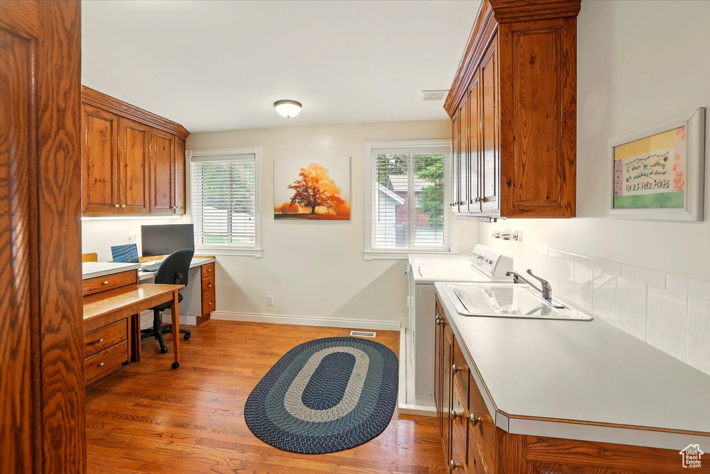 Laundry room featuring cabinet space, light wood-style flooring, an office area, and baseboards