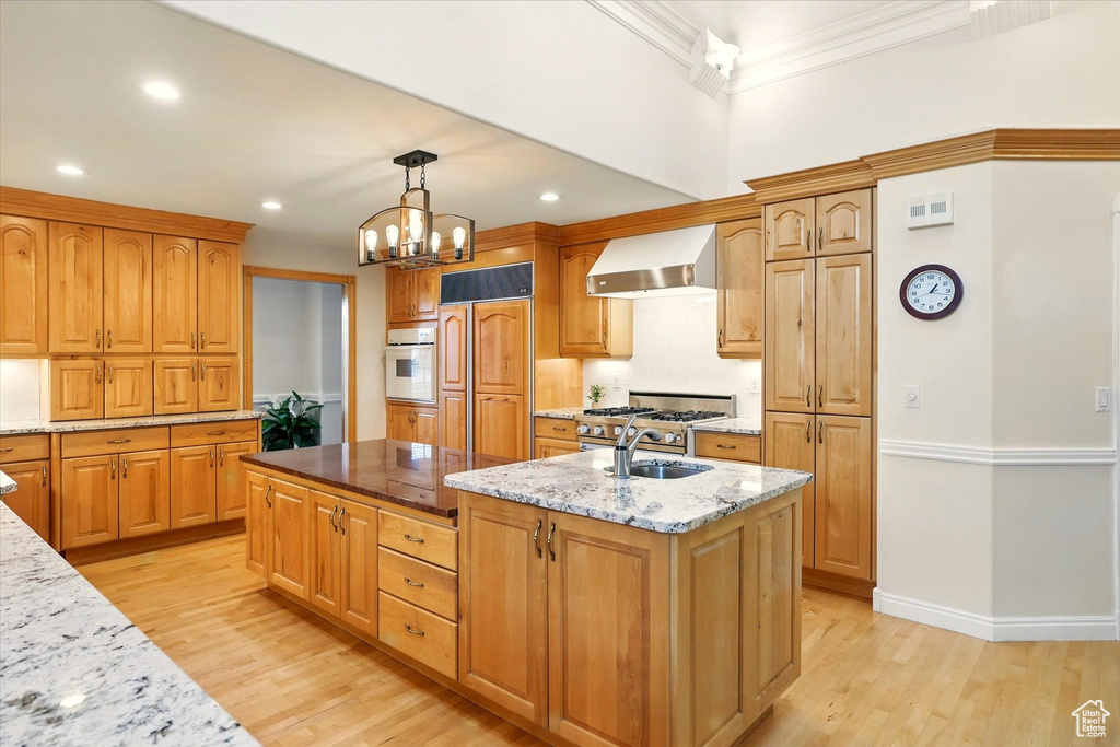 Kitchen with wall chimney exhaust hood, oven, crown molding, paneled built in refrigerator, and a center island with sink