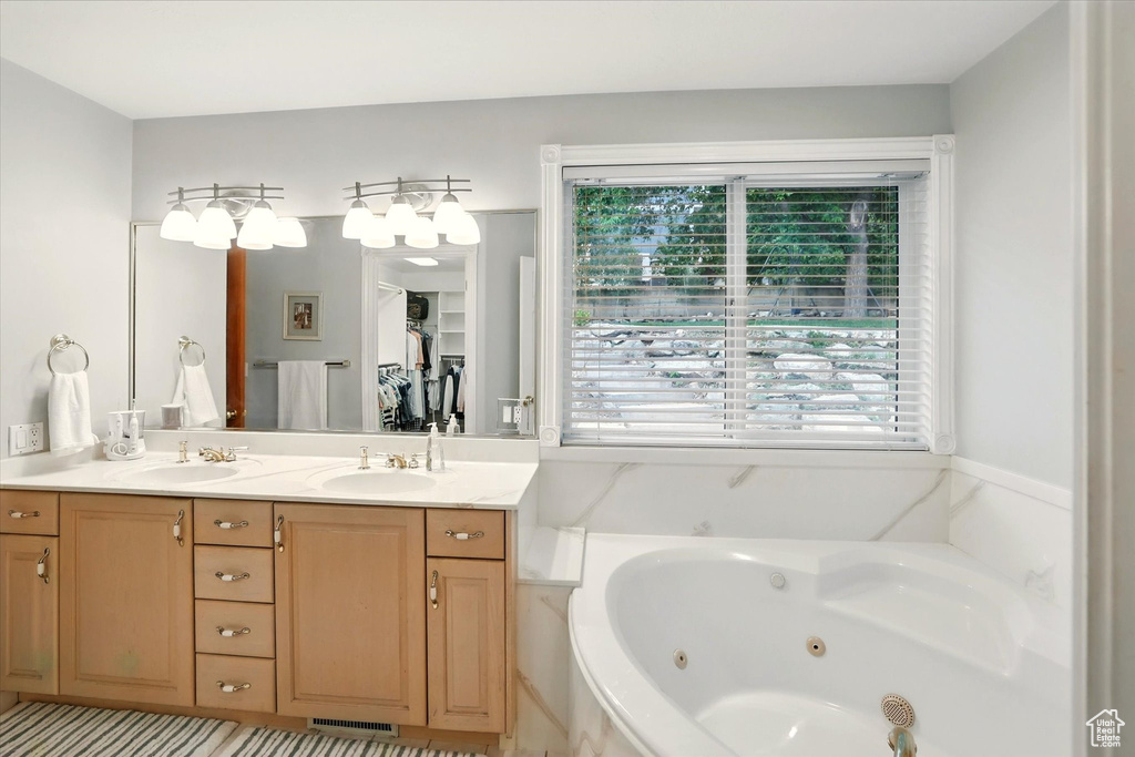 Full bath featuring healthy amount of natural light, a jetted tub, and double vanity