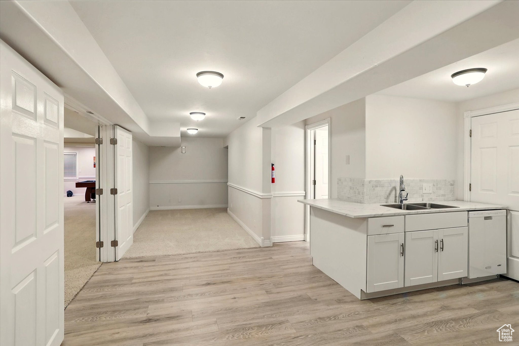 Kitchen featuring a sink, white dishwasher, light wood-style floors, decorative backsplash, and white cabinetry