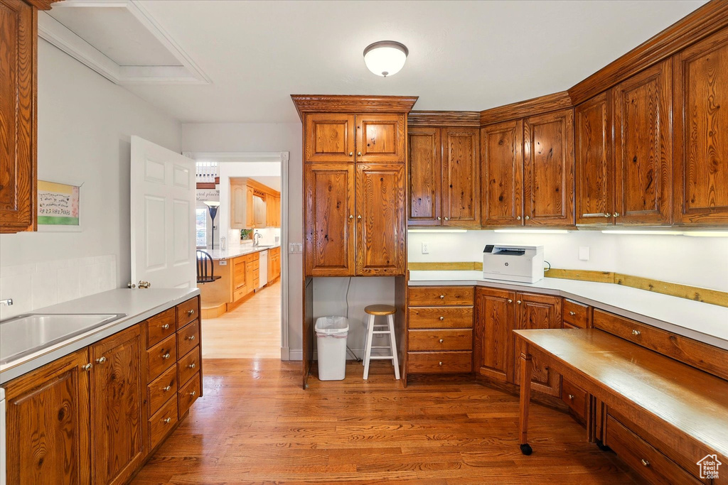 Kitchen featuring wood finished floors, brown cabinetry, light countertops, a sink, and white dishwasher