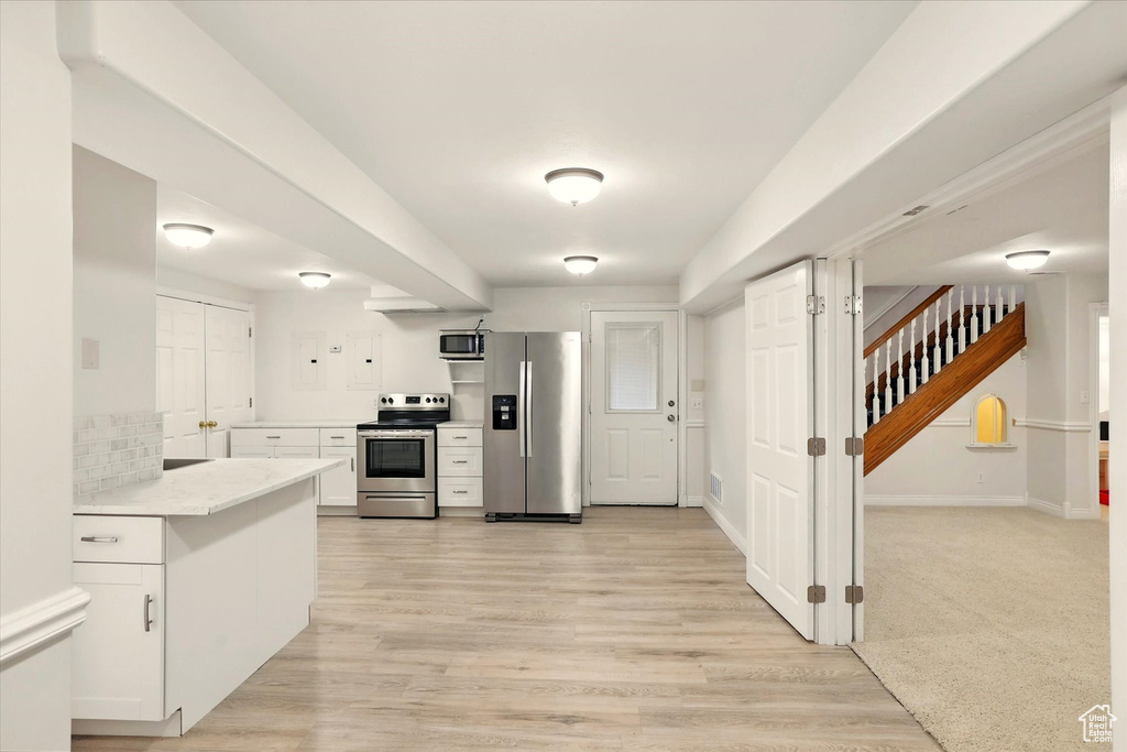 Kitchen featuring appliances with stainless steel finishes, white cabinets, light countertops, and light wood-style floors