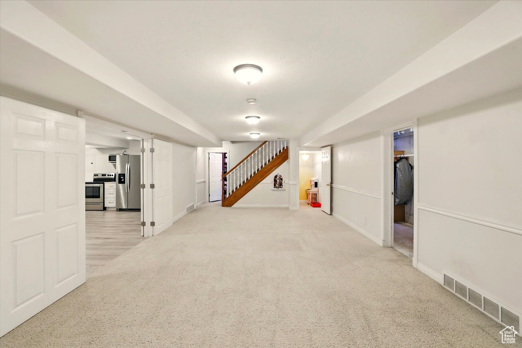 Finished below grade area featuring stainless steel fridge with ice dispenser, stairs, baseboards, and light colored carpet