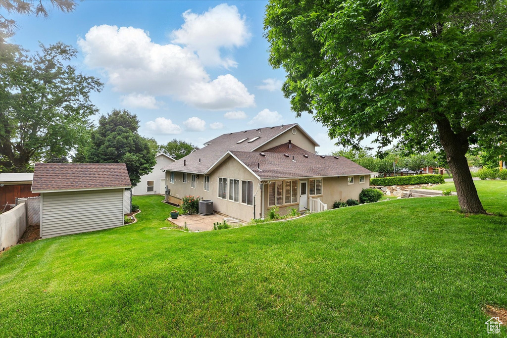 Rear view of property with a patio, a lawn, an outdoor structure, a sunroom, and central AC unit