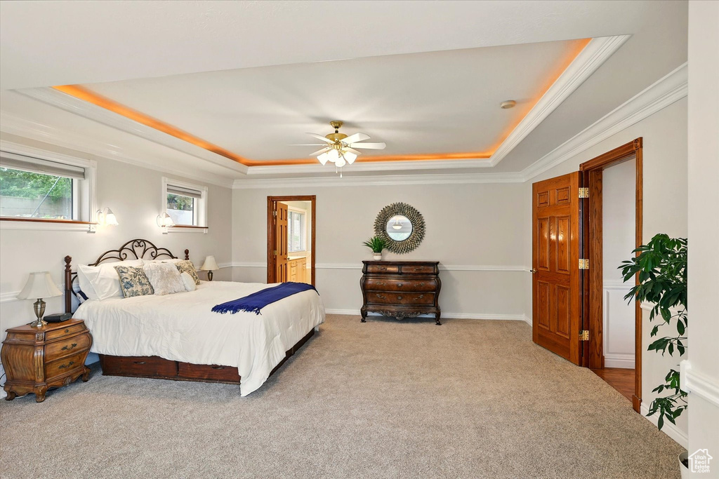 Bedroom with a raised ceiling, carpet flooring, crown molding, connected bathroom, and a ceiling fan