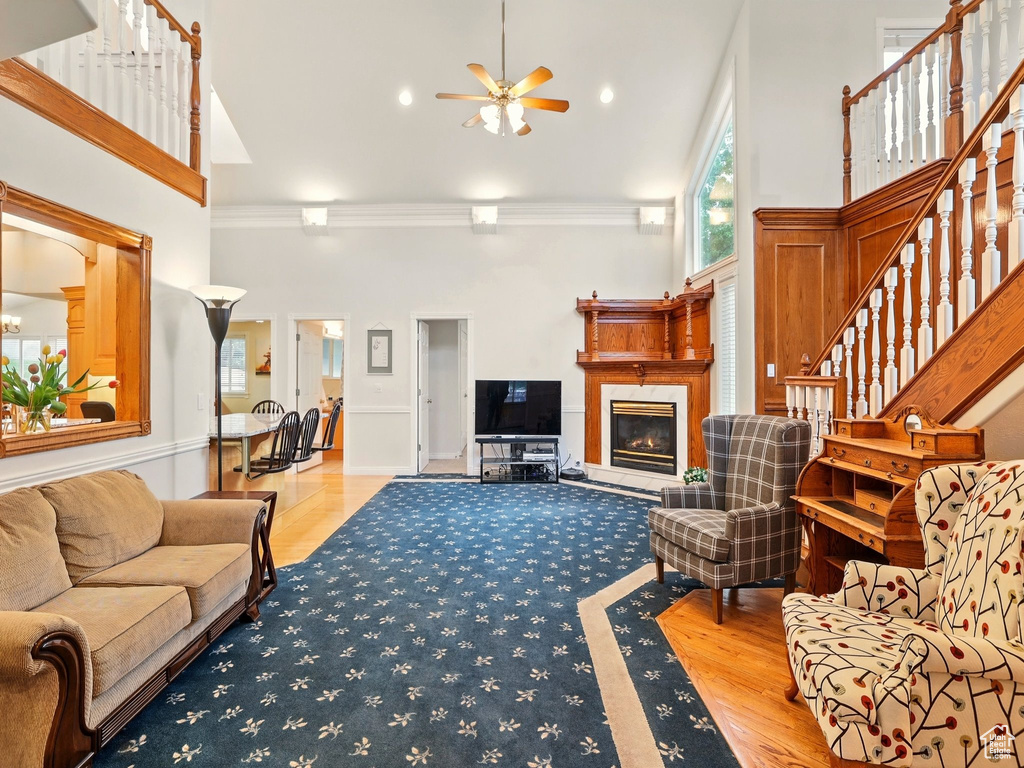 Living area featuring ceiling fan, crown molding, a towering ceiling, a glass covered fireplace, and stairway