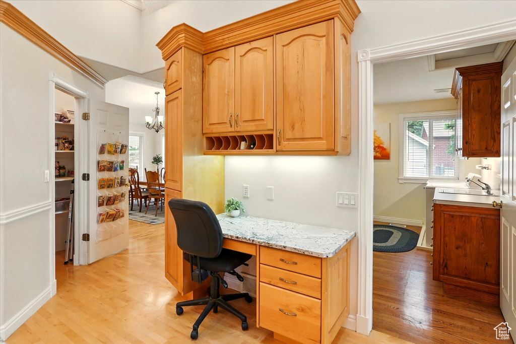 Office space featuring light wood-style flooring, a sink, a chandelier, built in desk, and baseboards