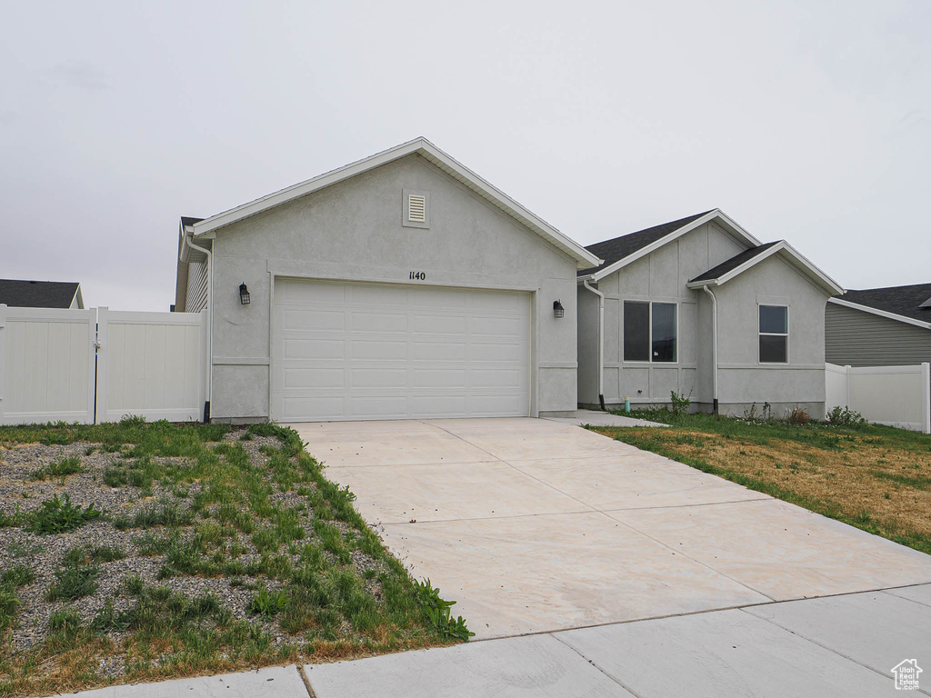 Single story home featuring stucco siding, fence, a garage, driveway, and a gate